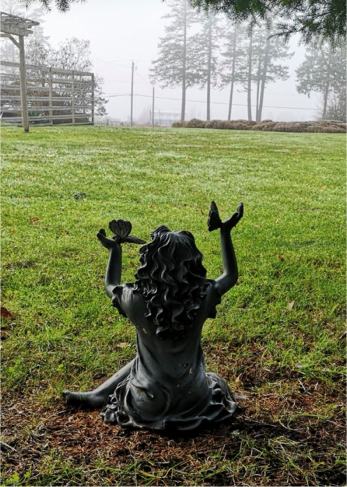 A sculpture of a girl sitting with hands raised, seen from the back
